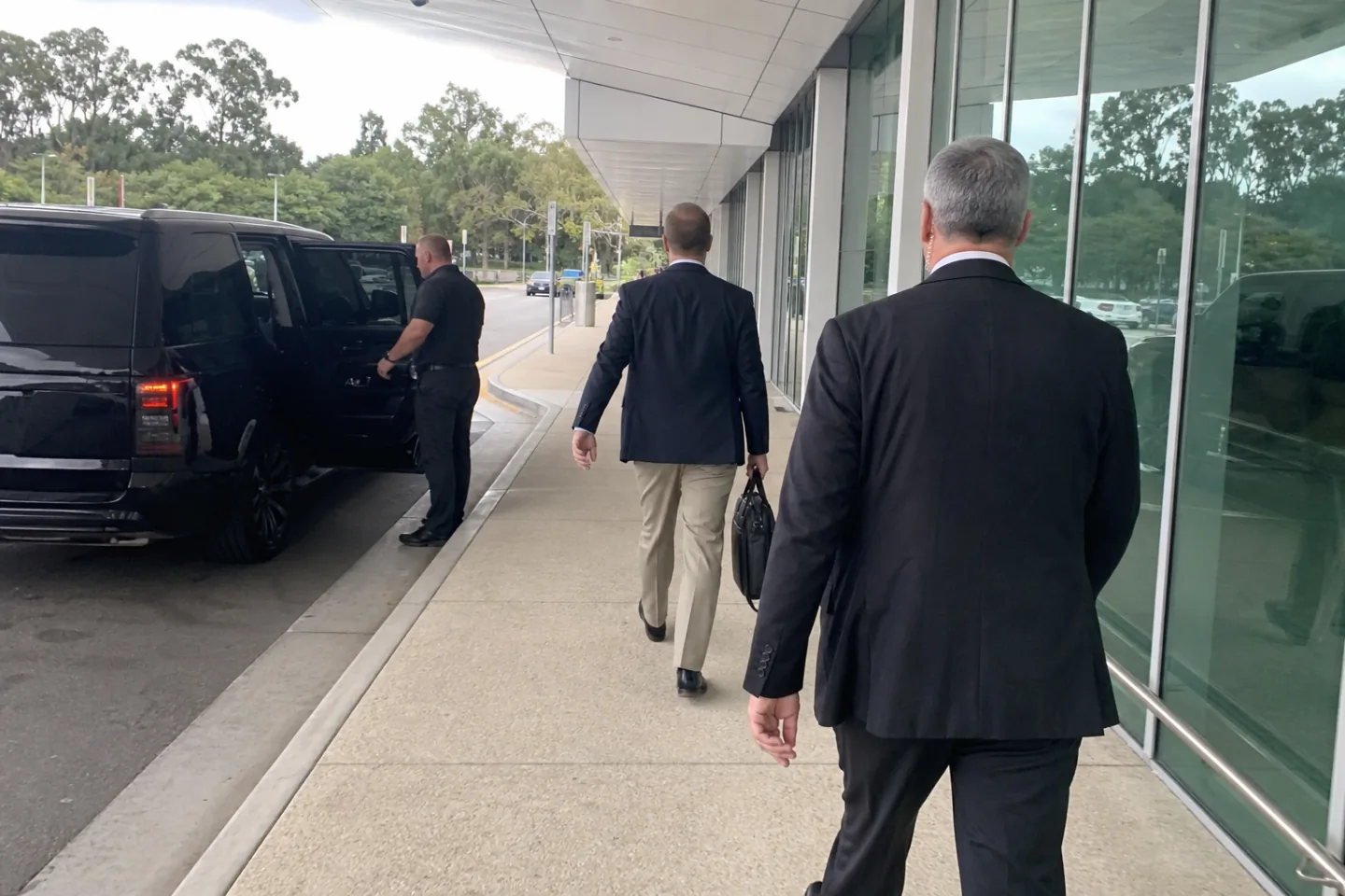 Close protection operator walking a principal to a vehicle at an airport kerb