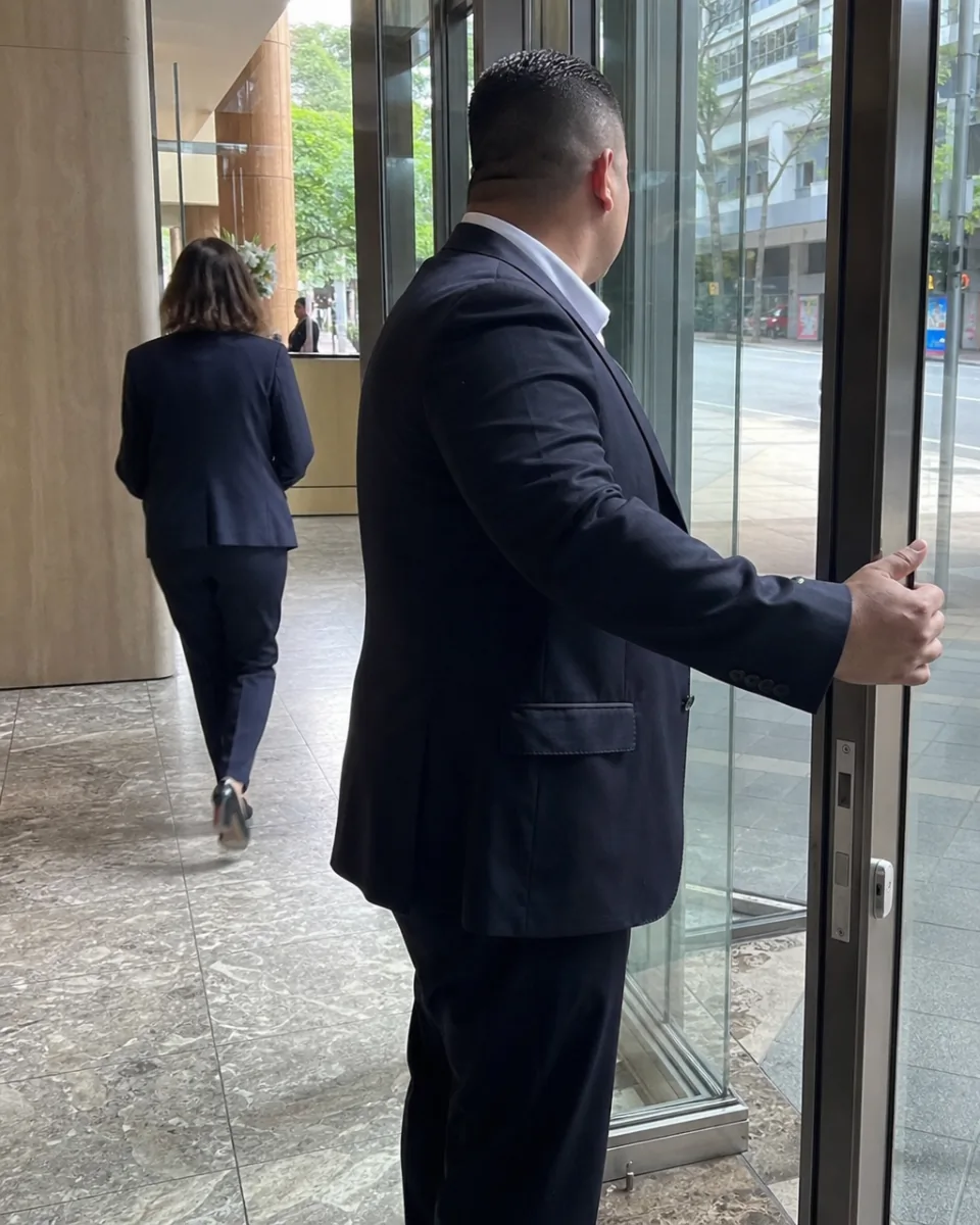 Close protection operator holding a Brisbane office lobby door for a principal